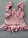 Front view of a girls pink and white tie-dye smocked tank top with ruffle shoulder straps, suitable for youth kids aged 7 to 15.