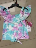 Flat lay display of Justice girls cold-shoulder ruffle tops in vibrant sunset pink and ocean blue tie-dye styles