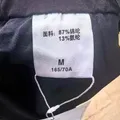Fabric care label showing 87% polyamide and 13% elastane composition on men's casual pants wholesale stock