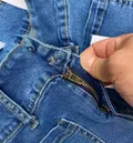 Close-up of waistband, button closure, and front pocket on denim jeans